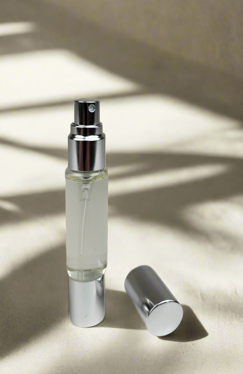 Small glass spray bottle with silver cap on a light background