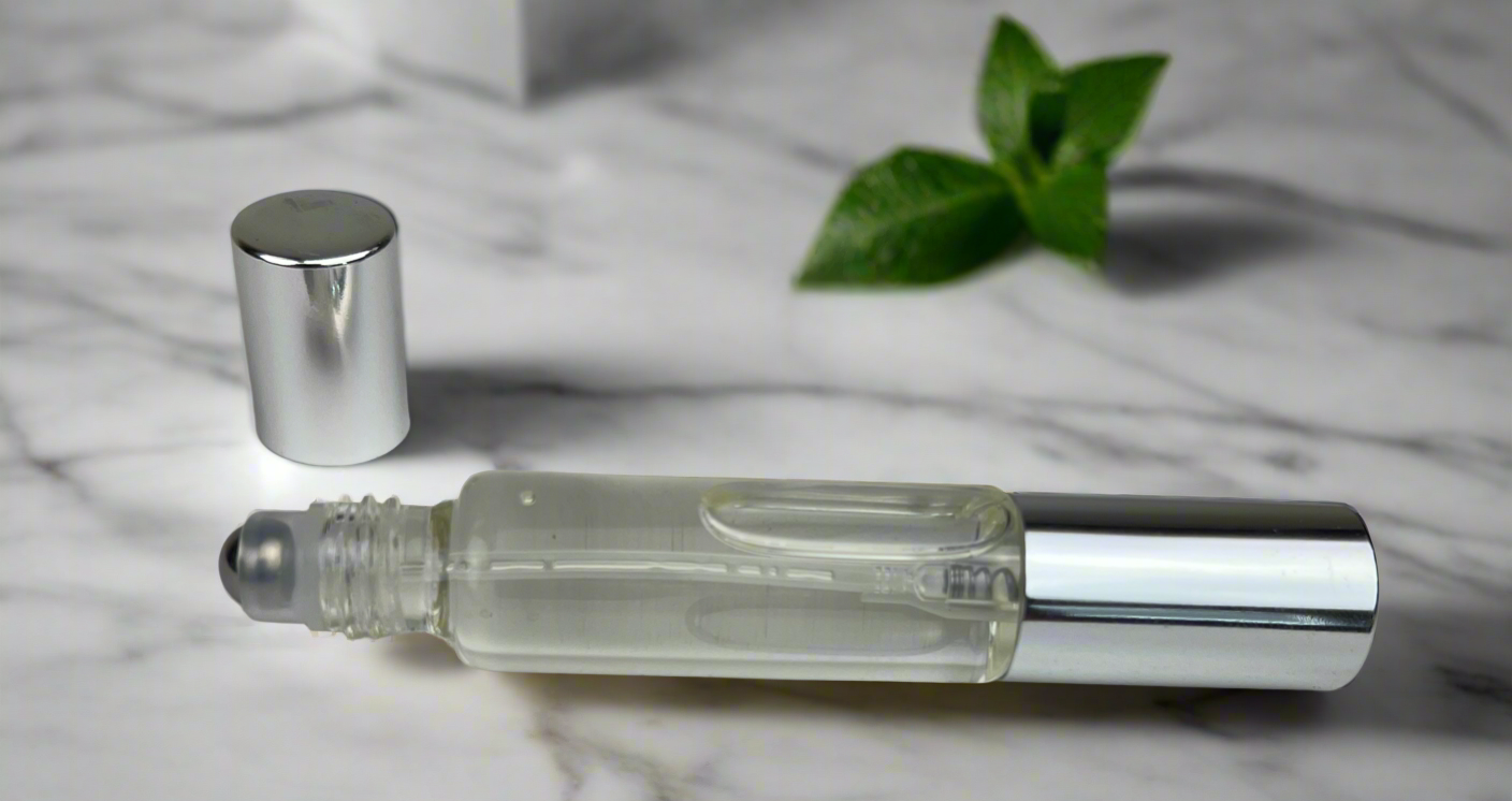 Clear glass rollerball bottle with silver cap on a marble surface with green leaves.