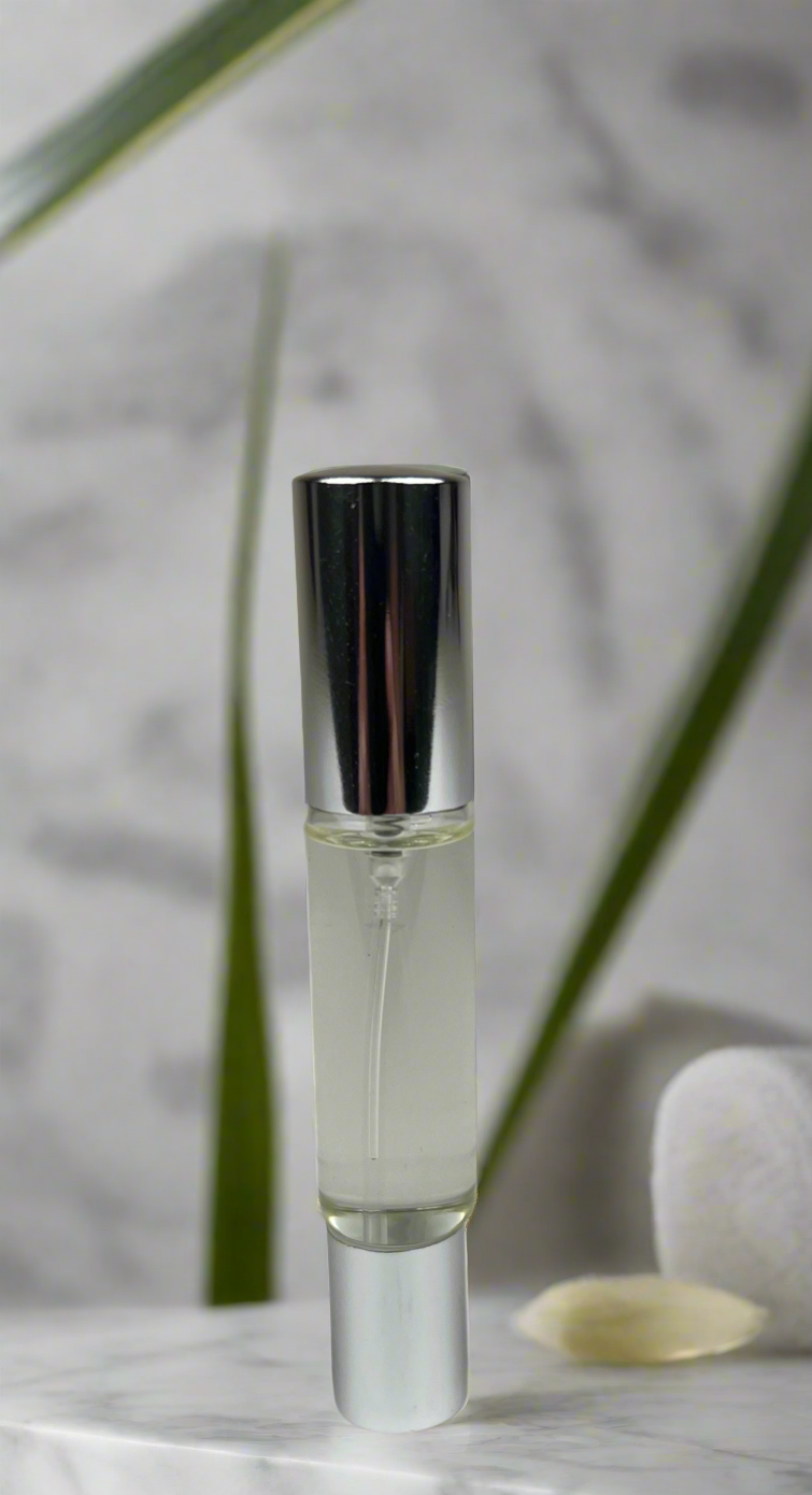 Clear glass rollerball with silver cap on a marble surface with green leaves in the background